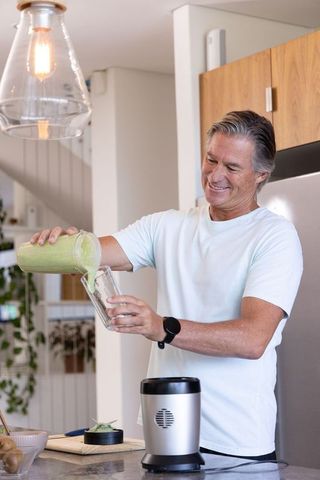 Senior man pouring green smoothie in modern kitchen, enjoying healthy lifestyle