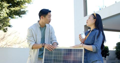 Asian couple installing solar panel on rooftop while discussing sustainable home energy