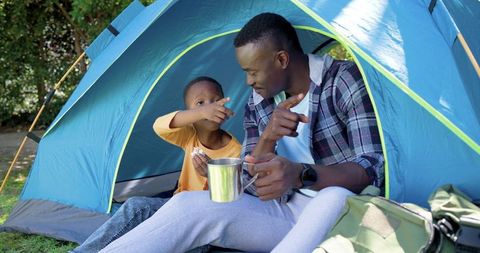 African american father and son camping in blue tent sharing morning coffee and bonding