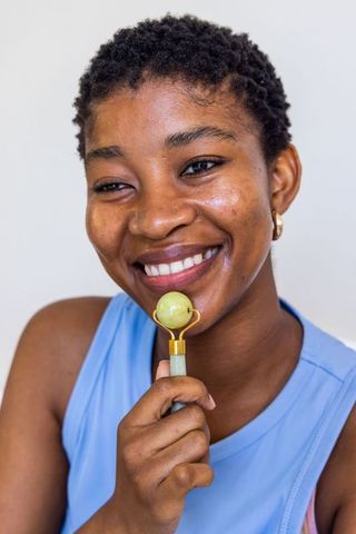 African woman using jade facial roller smiling closeup beauty skincare routine