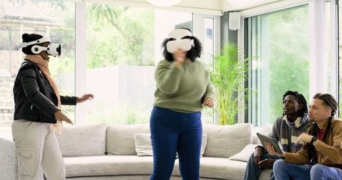 Diverse friends wearing white VR headsets and using tablet in sunlit modern living room