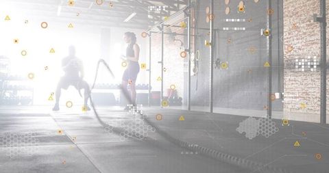 Backlit duo swinging battle ropes in industrial gym for high-intensity strength training