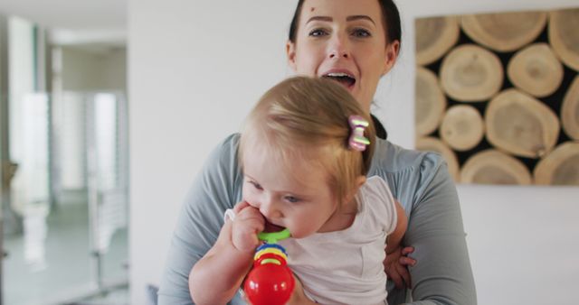 A mother is smiling while holding her baby who is chewing on a teething toy. This can be used to illustrate family bonding, parenting, childcare, or advertising baby products. Ideal for websites and promotions related to family life or parenting tips.