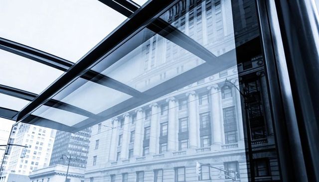 Glass canopy reflecting classical stone facade on downtown street with traffic light