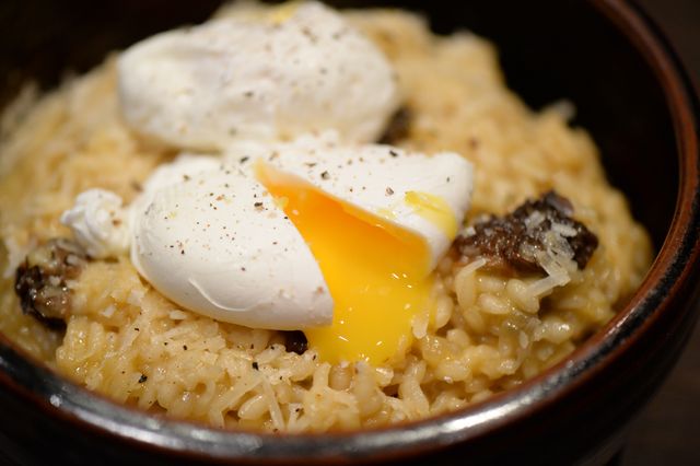 Close-up view of gourmet risotto topped with poached eggs and a drizzle of truffle oil. The broken yolk adds a rich, creamy texture, making it a luxurious dining experience. Ideal for food blogs, restaurant menus, culinary magazines, and social media posts showcasing high-quality dining.