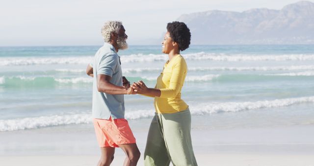 Happy african american couple dancing and holding hands on sunny beach. healthy and active time beach holiday.