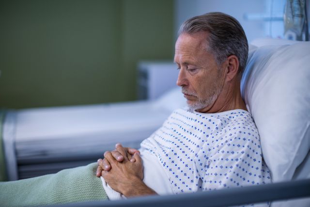 Elderly man sitting on a hospital bed, appearing thoughtful and contemplative. Perfect for use in healthcare, medical and senior care advertisements or articles discussing patient recovery, hospital experiences and treatment of illnesses in older adults.
