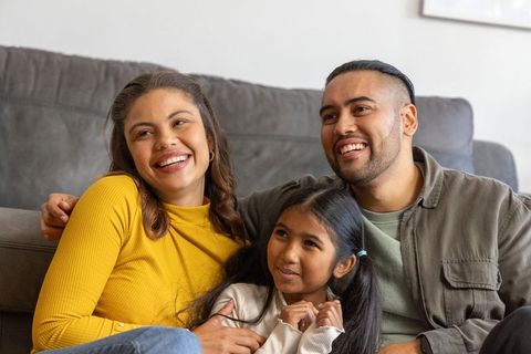 Smiling family cuddling on couch enjoying cozy home time, parents with young daughter