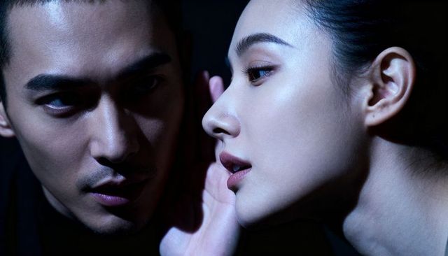 Woman whispering into man's ear closeup portrait in dramatic chiaroscuro lighting