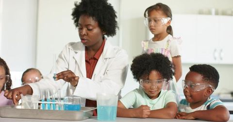 Diverse teacher leading children performing hands-on chemistry experiment with blue liquid