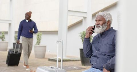 Senior african american man talking on phone at transit plaza with silver luggage