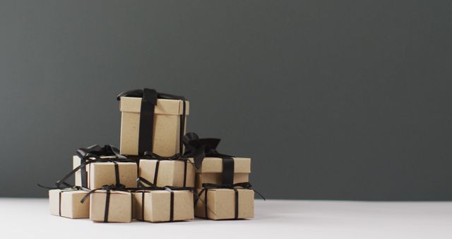 Stacked gift boxes with black ribbons against dark background provide minimalist aesthetic. Suitable for holiday promotions, packaging design, birthday celebrations, and event material. Useful for marketing campaigns and invitations.