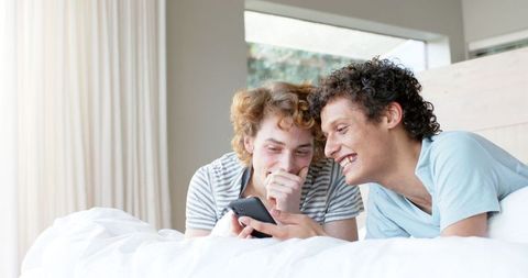 Happy Male Couple on Bed Enjoying Smartphone Together