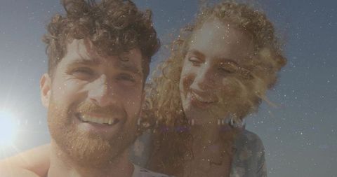 Smiling couple leaning close at beach with sun flare, sunlit warmth and film grain