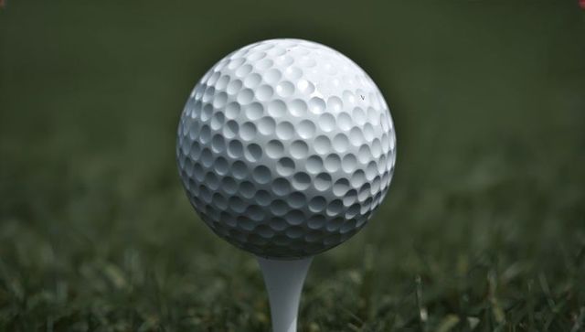White dimpled golf ball resting on tee over green grass macro closeup with scuff