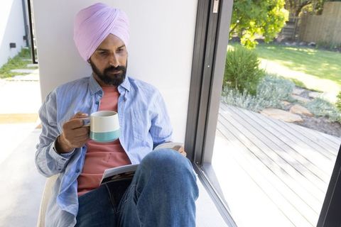 Sikh man relaxing with mug and smartphone by window