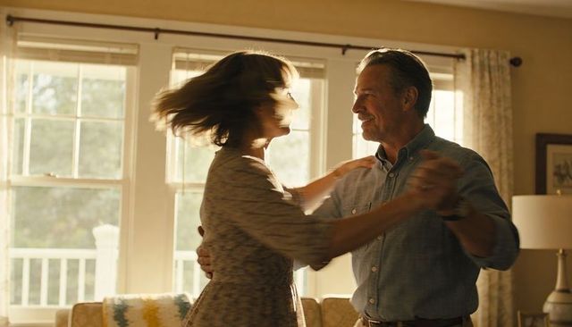 Middle-aged couple dancing in sunlit living room spinning with joy and warmth