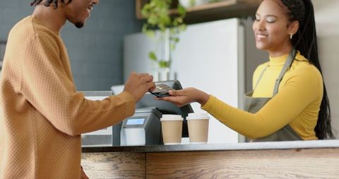 African american barista serving customer while tapping contactless payment at cafe
