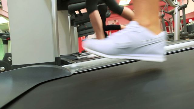 Scene shows individuals running on treadmills in a gym, focusing on lower bodies and sneakers. This context indicates active lifestyle, encouraging fitness and well-being. Useful for illustrating healthy living, gym equipment, or workout regimens in fitness-related materials, advertisements, or wellness blogs.