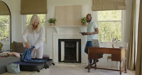 Diverse Couple Packing Suitcase and Planning Vacation with Tablet
