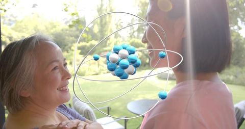 Sunlit intergenerational bond on patio with atom sculpture, smiling women sharing moment