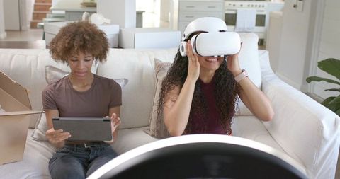 Two African American Women Using VR Headset and Tablet on Sofa Exploring Virtual Reality