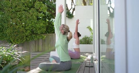 Women practicing seated yoga on sunlit deck for outdoor mindfulness and gentle stretching