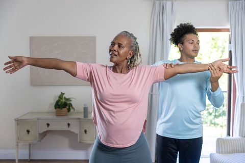 Senior african american woman doing assisted arm stretch at home with caregiver
