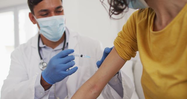 Hispanic male doctor making injection to girl at home, all wearing face masks,. medical professional making patient home visit during coronavirus covid 19 pandemic.