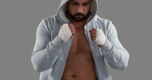 Mixed martial artist wrapped hands preparing for training. Gray hoodie open to reveal muscular physique implies focus and determination. Ideal for use in fitness, sports, personal training, and martial arts promotion.