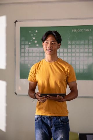 Asian teen student holding tablet presenting lesson with periodic table background