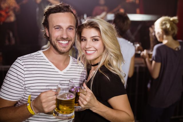 Portrait of smiling young friends holding beer mugs at nightclub