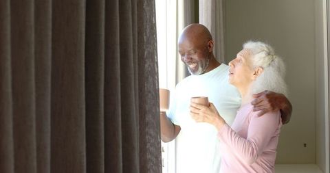 Diverse senior couple enjoying coffee by sunlit window