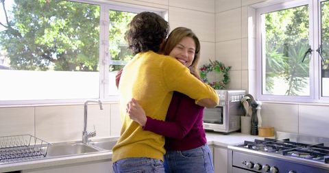 Couple hugging and smiling in sunlit modern kitchen, cozy home embrace and togetherness