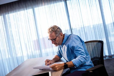 Senior Businessman Reviewing Documents by Desk in Bright Office