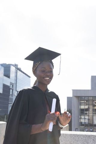 Young black graduate celebrating academic achievement on city rooftop holding diploma