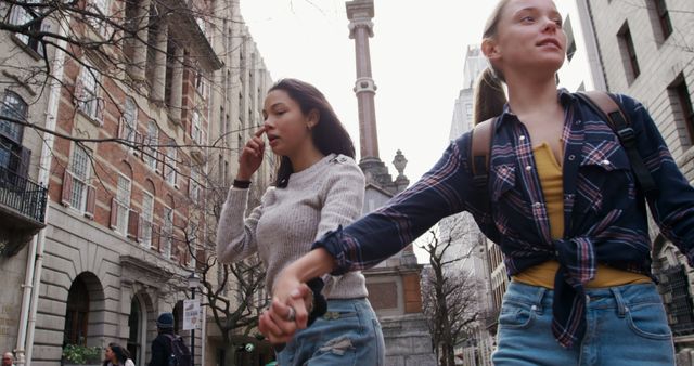 Diverse girl friends walking holding hands in city, copy space. Summer, friendship, on the go, city and lifestyle concept, unaltered.