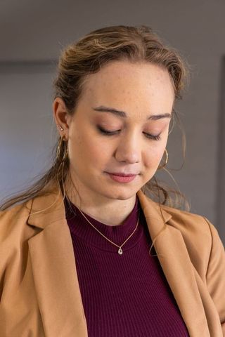 Contemplating young professional wearing tan blazer and burgundy top with pendant