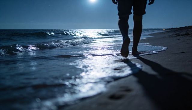Moonlit Beach Walking: Barefoot Silhouette Strolling Along Ocean Shoreline at Night