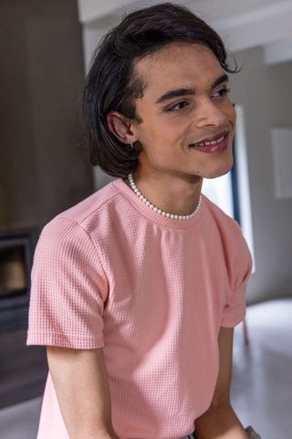 Indian man leaning and smiling in pink shirt and pearl necklace in minimalist home