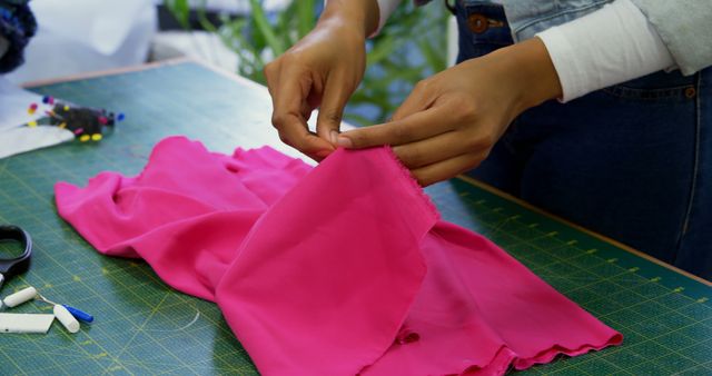 African American hands are shown sewing a vibrant pink fabric on a table scattered with sewing tools, with copy space. Sewing is a skillful activity that often reflects creativity and attention to detail in garment making.