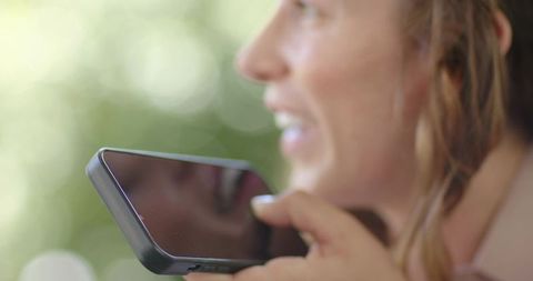 Speaking into smartphone for voice message outdoors with reflective screen and bokeh