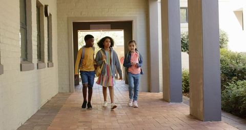 Teen students walking campus corridor carrying backpacks and checking smartphone