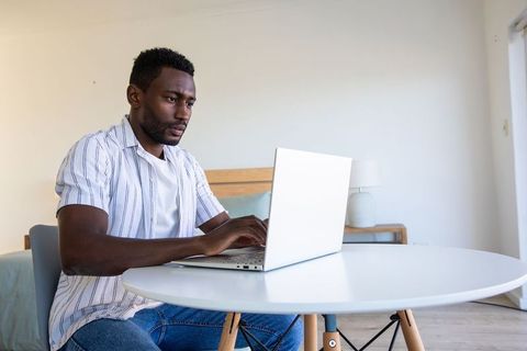 Focused Man Typing on Laptop in Minimalist Bedroom Workspace