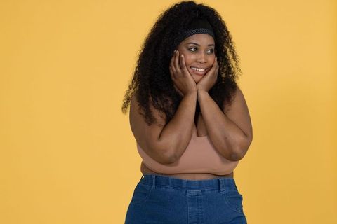 African american woman smiling and posing with hands on cheeks on vibrant yellow backdrop