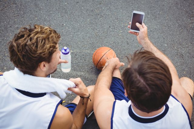 Overhead view of basketball players using smart phone while sitting in court