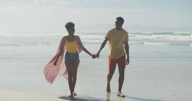 African american couple holding hands smiling while walking on the beach. family travel and vacation concept