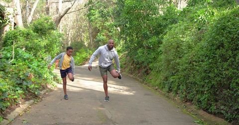 African american father and son stretching on forested park trail for running warmup