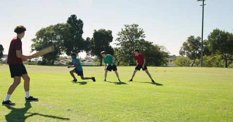 Teen friends playing casual baseball in sunny park field, diving, catching and batting