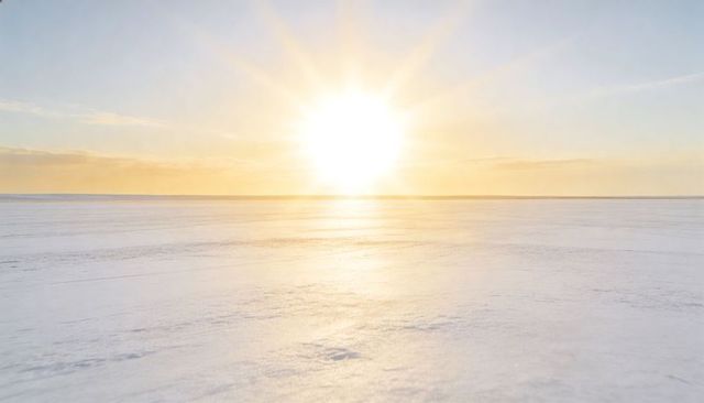 Shining arctic sun casting golden glare across minimal snow plain on vast frozen horizon